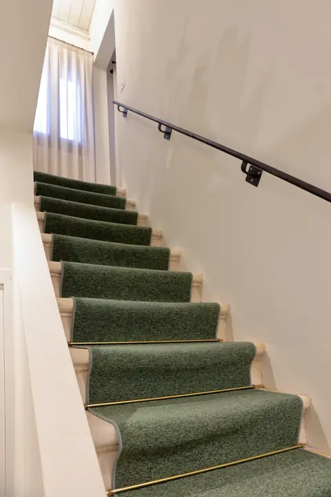 Escalera con moqueta verde y varillas de latón